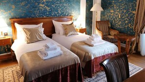 Hotellihuone, jossa on kaksi sänkyä, puinen pääty, tuoli ja pieni pöytä.