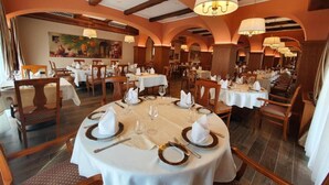 Ein Restaurant mit runden Tischen, gedeckt mit weißen Tischdecken, goldenen Tellern und ordentlich platzierten Besteck.