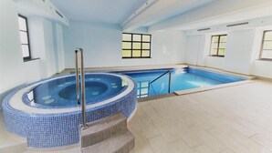 En indendørs swimmingpool med jacuzzi, flisegulv og vinduer.