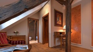 Un dormitorio acogedor en el ático con techo de madera, un escritorio con lámpara, una silla y una cama.