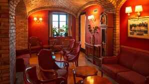 Une pièce chaleureuse avec des arches en briques, des murs rouges et des meubles en bois. On y trouve deux fenêtres avec des rideaux, une cheminée et un tableau accroché au mur.