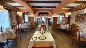 Une grande salle à manger avec des tables dressées, des poutres en bois au plafond et un grand tableau accroché au mur.
