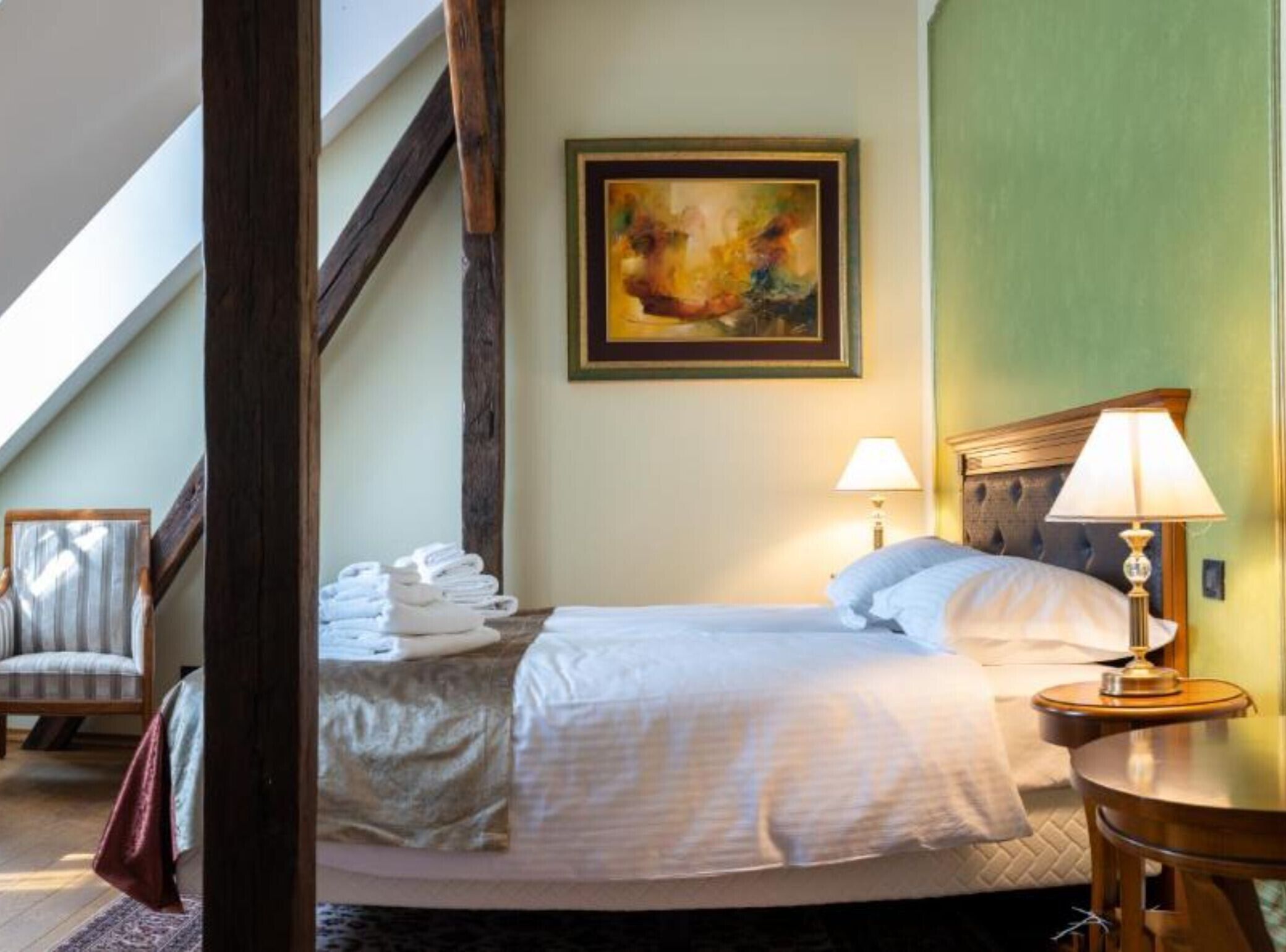 Une chambre d’hôtel avec un lit, un tableau au mur, une chaise et une table avec une lampe.