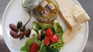 Een bord met salade, olijven, brood en een pot augurken.