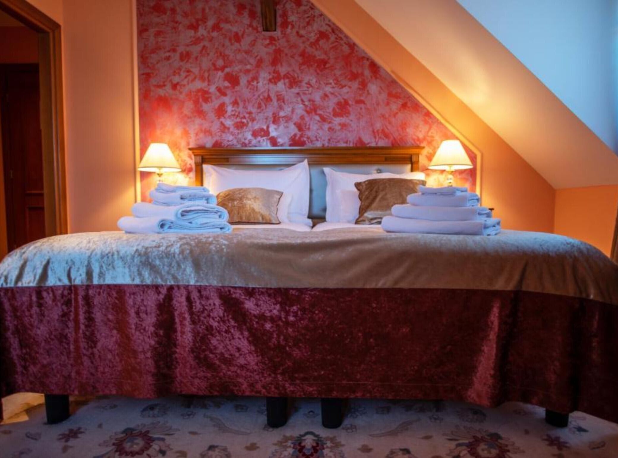 A hotel room with a bed, two bedside lamps, and towels.