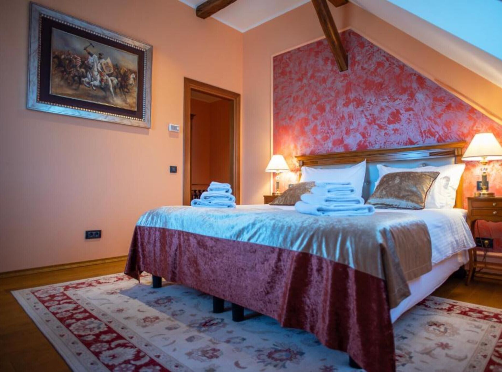 Een hotelkamer met een bed, twee bedlampen, een schilderij aan de muur en een rode, patroonbehang muur.