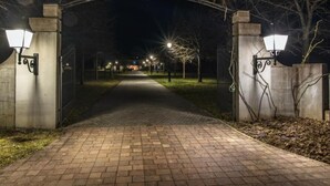 En lukket indgang med et skilt der viser "MORAC JUROFEJ", om natten, med gadelamper og en belagt sti, der fører til en bygning.