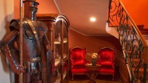 Une pièce avec un canapé rouge, une petite table sur laquelle est posé un vase, et un escalier doté de rampes décoratives.