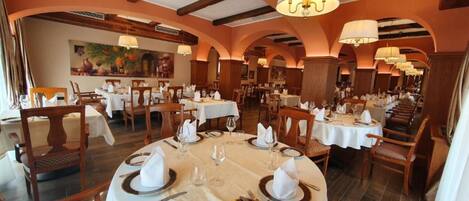 A restaurant with round tables set for dining, featuring white tablecloths, gold-rimmed plates, and neatly arranged cutlery.