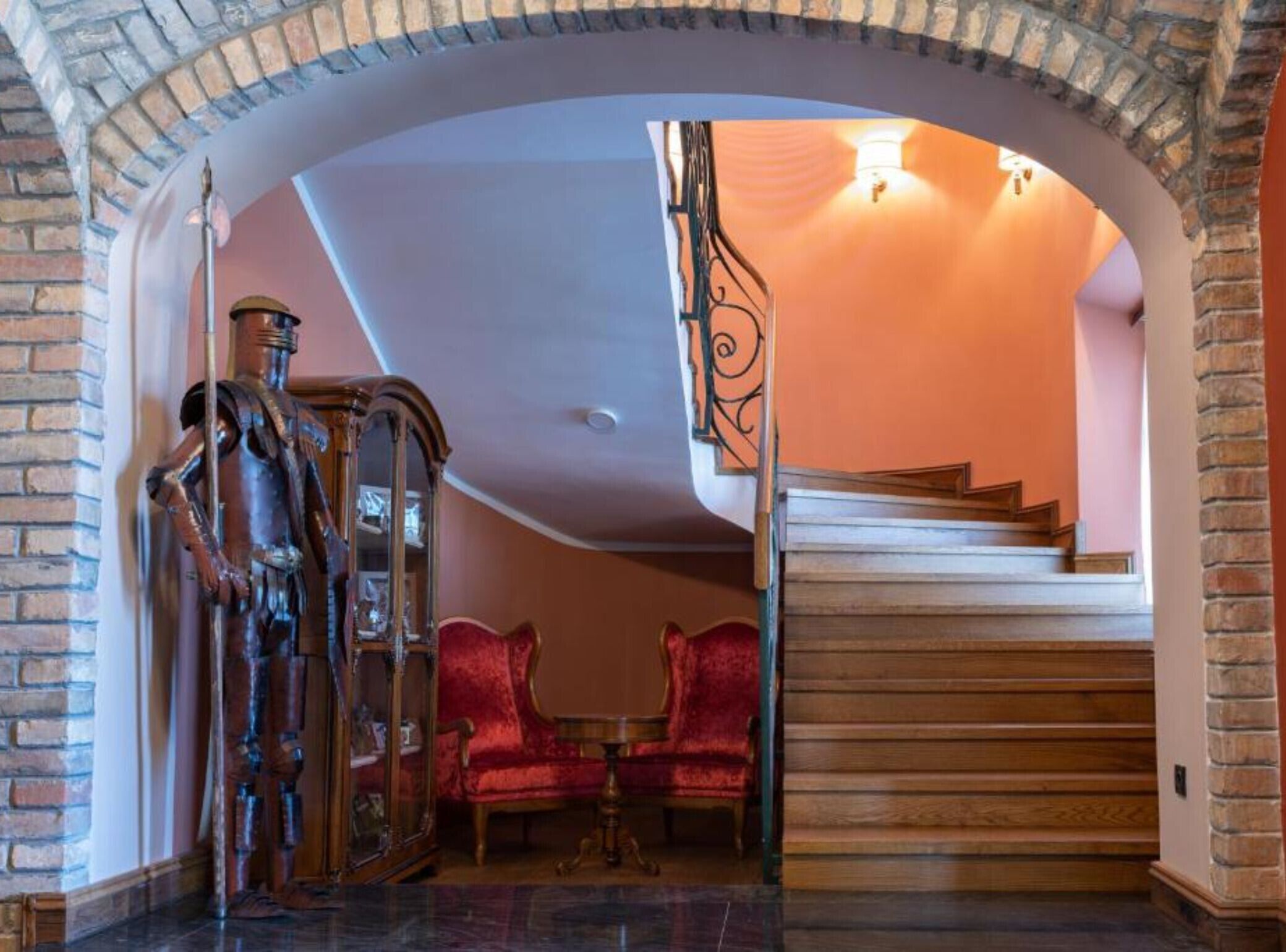 A grand staircase with a wooden finish and a red velvet chair in the foreground.