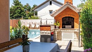 A poolside area with a table, chairs, and a brick oven. - Apartments Foric - Two bedroom apartment (1) (Rab)