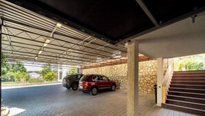 A covered parking area with two cars parked, a stone wall, and a staircase leading to an upper level. - Apartments Foric - Two bedroom apartment (1) (Rab)