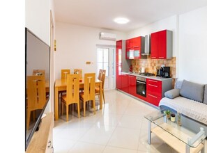A modern kitchen with red cabinets, a dining area with wooden chairs, and a glass coffee table. - Apartments Foric - Two bedroom apartment (2) (Rab)