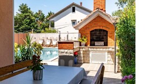 Uma área junto à piscina com mesa, cadeiras e um forno de tijolos.