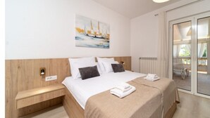 Quarto de hotel moderno com uma cama grande, cabeceira de madeira, pintura de veleiros, radiador e porta de vidro deslizante para uma varanda.