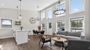 A spacious living area with a large window, a dining table, and a gray sofa. - Basecamp | Beach Access | Sports Court | Foosball (Invermere)