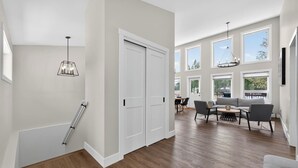 A spacious living area with a dining set, large windows, and a staircase. - Basecamp | Beach Access | Sports Court | Foosball (Invermere)