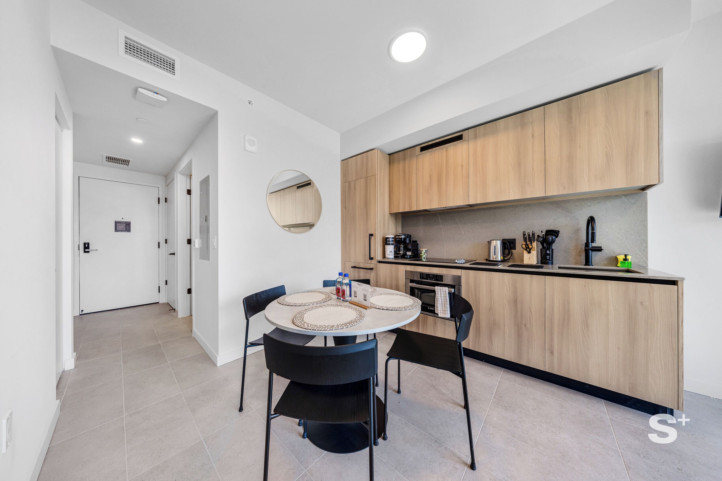 A modern kitchen with wooden cabinets, a round dining table with black chairs, and a small island with a sink.