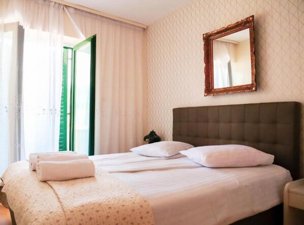 Habitación de hotel con una cama grande, cabecero, espejo y ventana con cortinas.