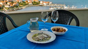 Ein Tisch mit einer Mahlzeit, einer Karaffe und zwei Gläsern vor einer malerischen Küstenansicht mit Blick auf das Wasser.