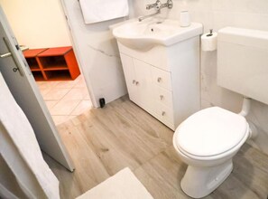 Une salle de bain avec des toilettes blanches, un lavabo et un meuble.