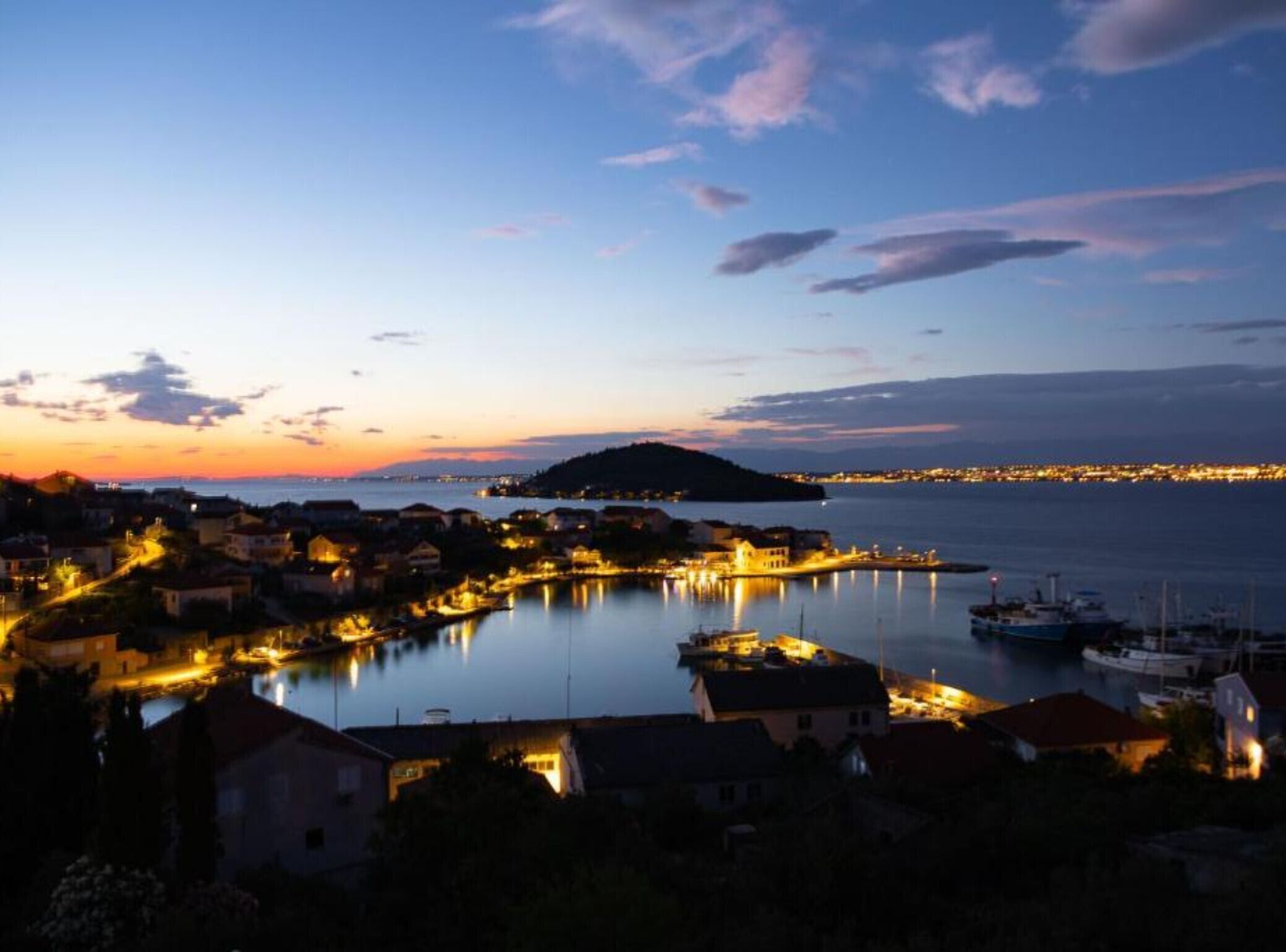 A coastal town at dusk with illuminated buildings and a calm sea.