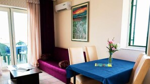 Een eethoek met een tafel bedekt met een blauwe tafelkleed, beige stoelen, een paarse bank en een schilderij aan de muur.