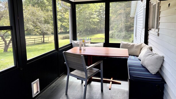 Un solárium con una mesa, un banco, ventanas amplias y vista a un jardín con césped.