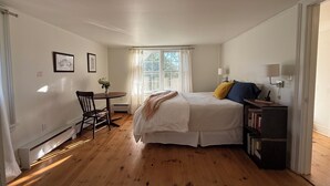 Un dormitorio con cama, mesita de noche, una silla, ventana con cortinas y una estantería.