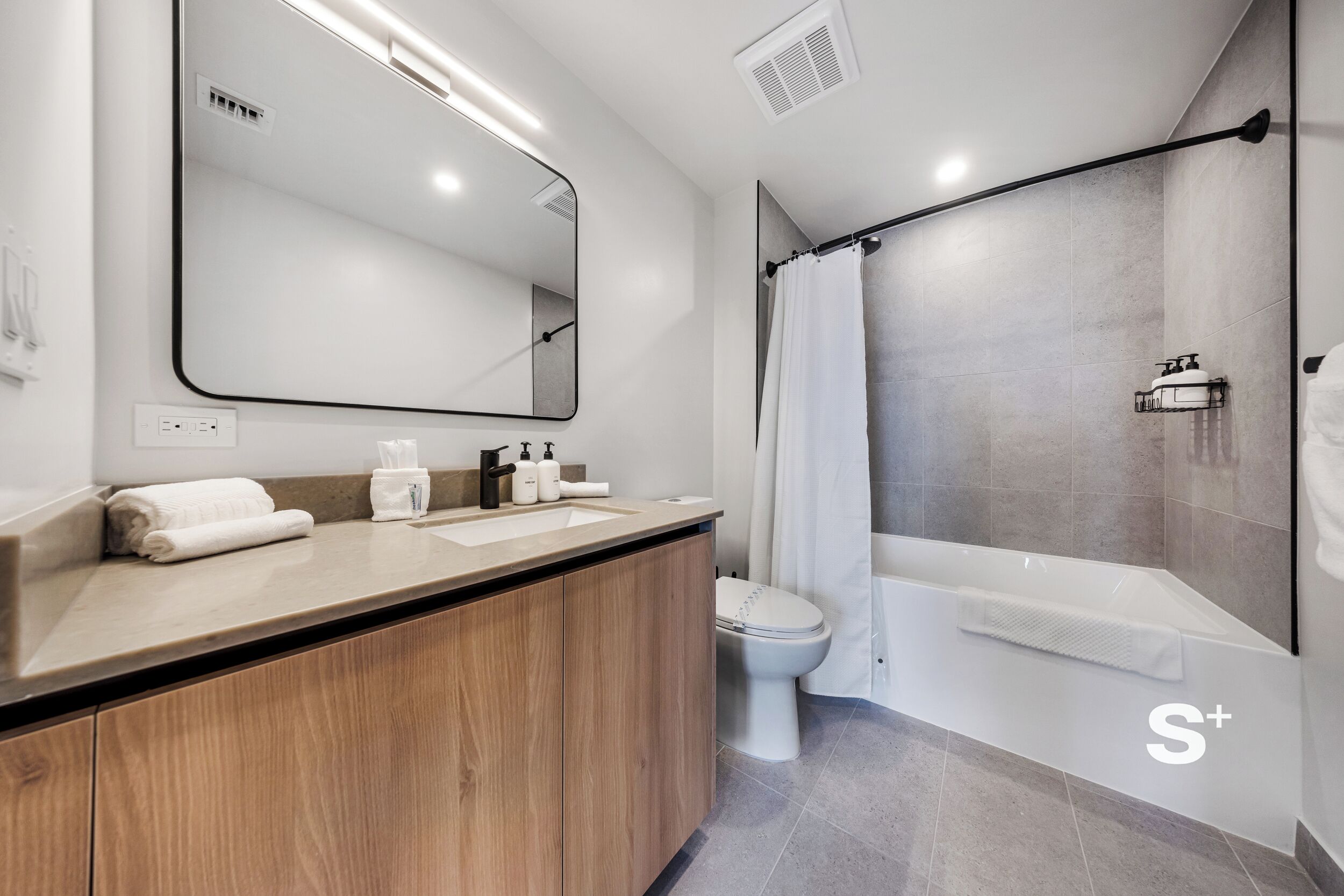 A modern bathroom with a wooden vanity, a large mirror, a toilet, and a walk-in shower.
