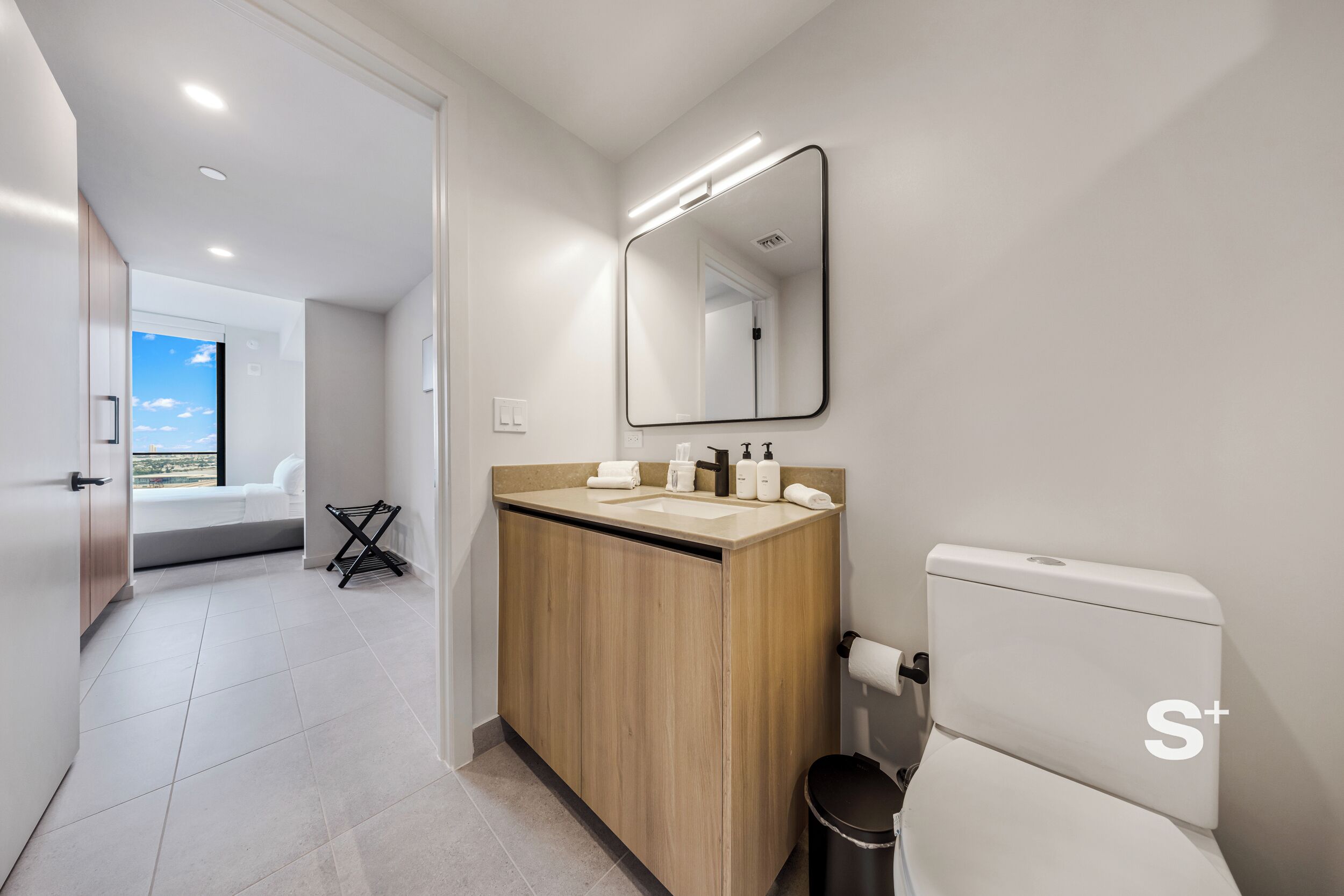A modern bathroom with a wooden vanity, a large mirror, and a toilet.