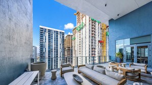 A modern rooftop lounge with a sofa, chairs, and a dining table, overlooking a cityscape with high-rise buildings. - High-Rise Miami Condo - Sea View (Miami)