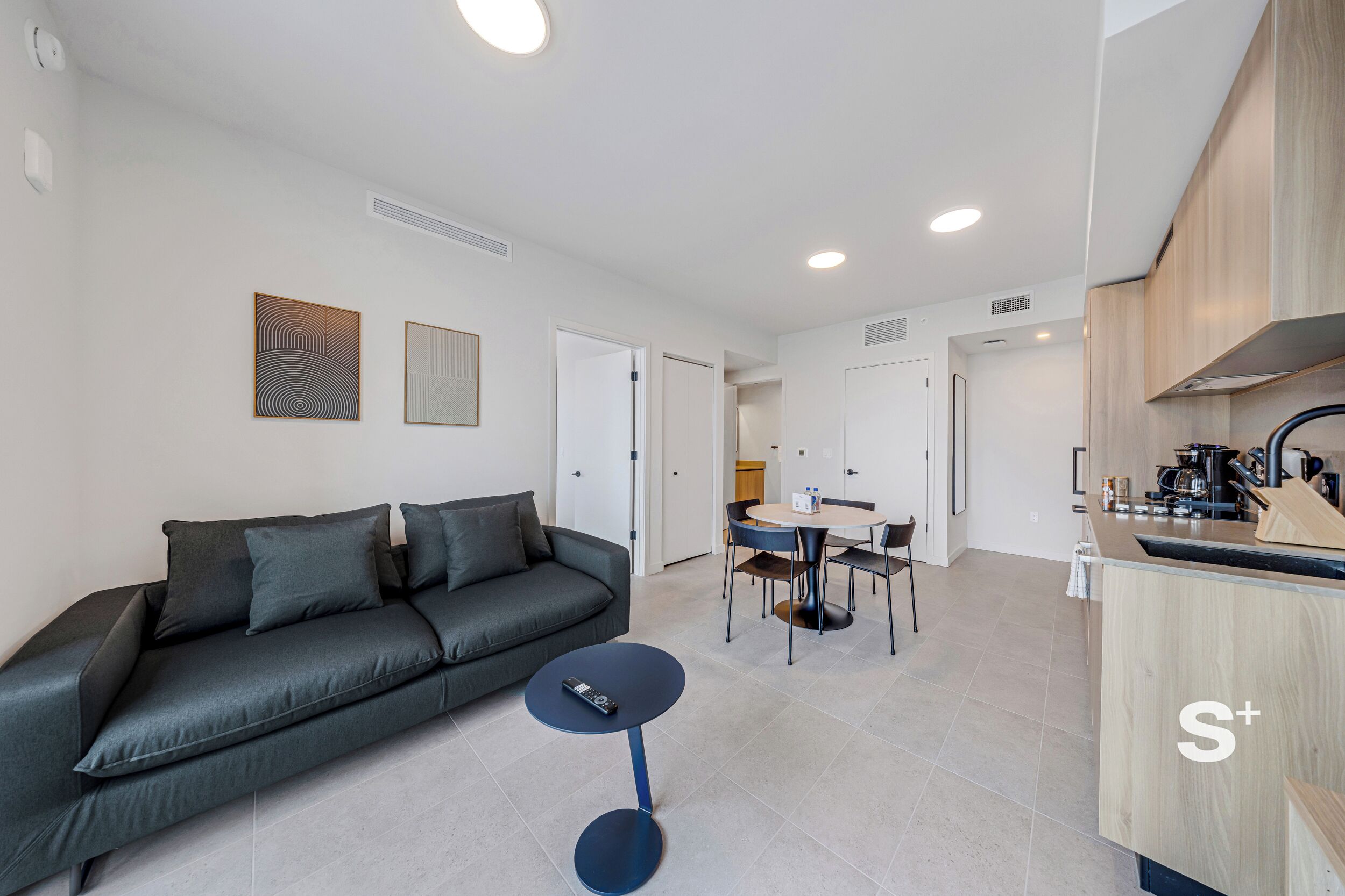 A modern living room with a sofa, a small round table, and a kitchen area with wooden cabinets and a sink.