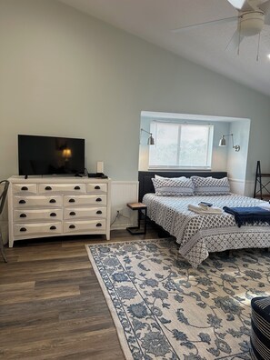 A bedroom with a bed, a dresser, a TV, a window with blinds, and a ceiling fan.