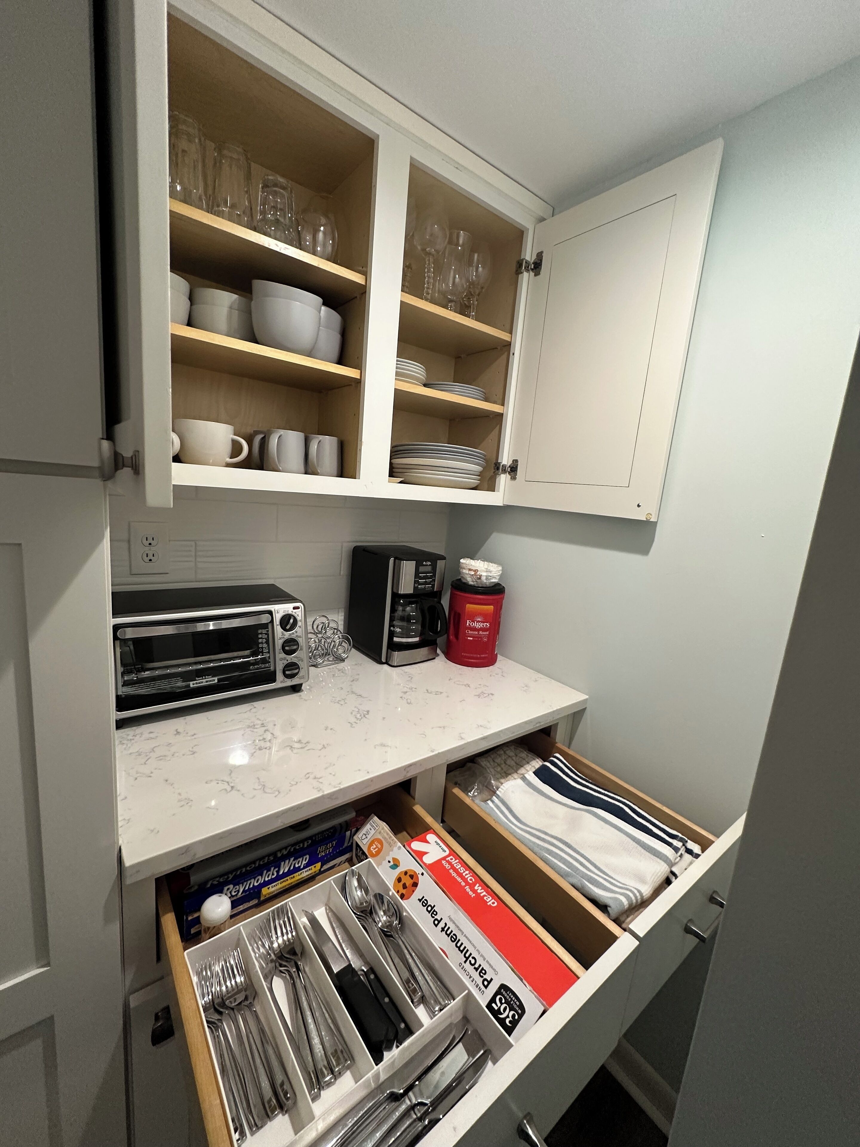 A kitchen with a microwave, toaster, coffee maker, and a drawer with utensils.