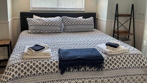 A neatly made bed with patterned bedding, a bedside lamp, and a window with blinds. - Beautiful remodeled studio across street to ocean SAWGRASS BEACH VILLAS (Sawgrass)