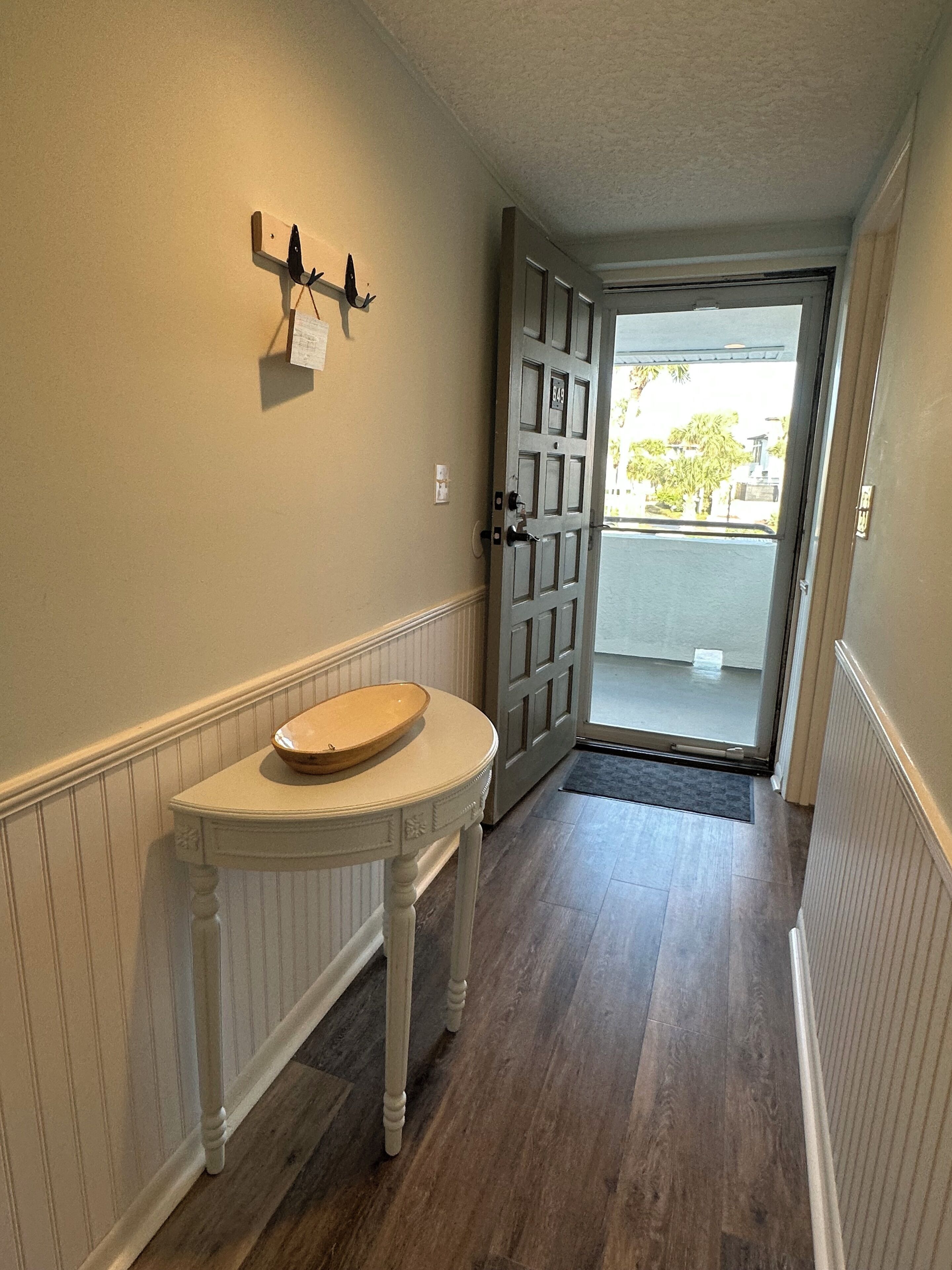 A hallway with a white table, a coat rack, and a door leading outside.