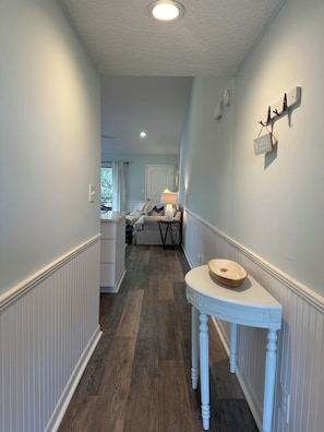 A hallway with a white vanity table, a door at the end, and a small table with a lamp.