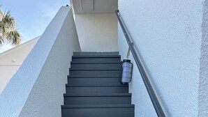 A set of dark wooden stairs leading up to a landing with a metal handrail and a lantern on the right. - Beautiful remodeled studio across street to ocean SAWGRASS BEACH VILLAS (Sawgrass)
