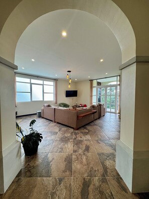 A spacious living area with a large sectional sofa, a flat-screen TV mounted on the wall, and a potted plant. - Escape the Cold- 2BR Mountain View Villa (Alajuela)