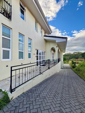 A building with multiple windows, a paved walkway, and a railing. - Escape the Cold- 2BR Mountain View Villa (Alajuela)