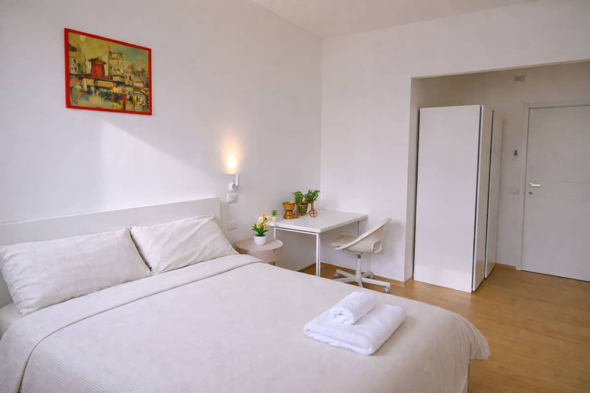 A neatly arranged hotel room with a bed, a desk, and a door.