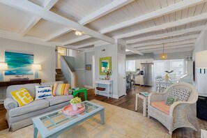 Ein geräumiges Wohnzimmer mit Sofa, Sessel und Couchtisch. Eine Treppe führt zu einer oberen Ebene.