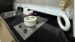 Una cocina con armarios de madera, encimera negra, pileta de acero inoxidable, microondas, tostadora y un florero decorativo con plantas secas.