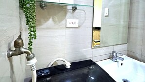 Un baño con un lavabo negro, un estante de vidrio con artículos de aseo, un espejo y una lámpara de pared.