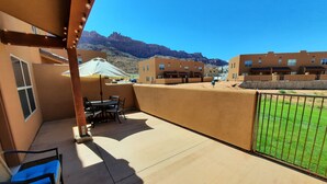 Eine Terrasse mit Tisch und Stühlen, ein überdachter Sitzbereich und im Hintergrund ein Wohnkomplex sowie Berge.