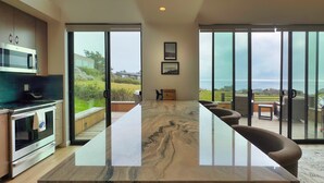 A modern kitchen with a large island, sliding glass doors, and a view of the ocean. - Sea Legacy | New Construction, Ocean View, Hot Tub (Sea Ranch)