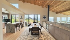 A modern kitchen with a marble island, wooden ceiling, and large windows offering ocean views. - Sea Legacy | New Construction, Ocean View, Hot Tub (Sea Ranch)