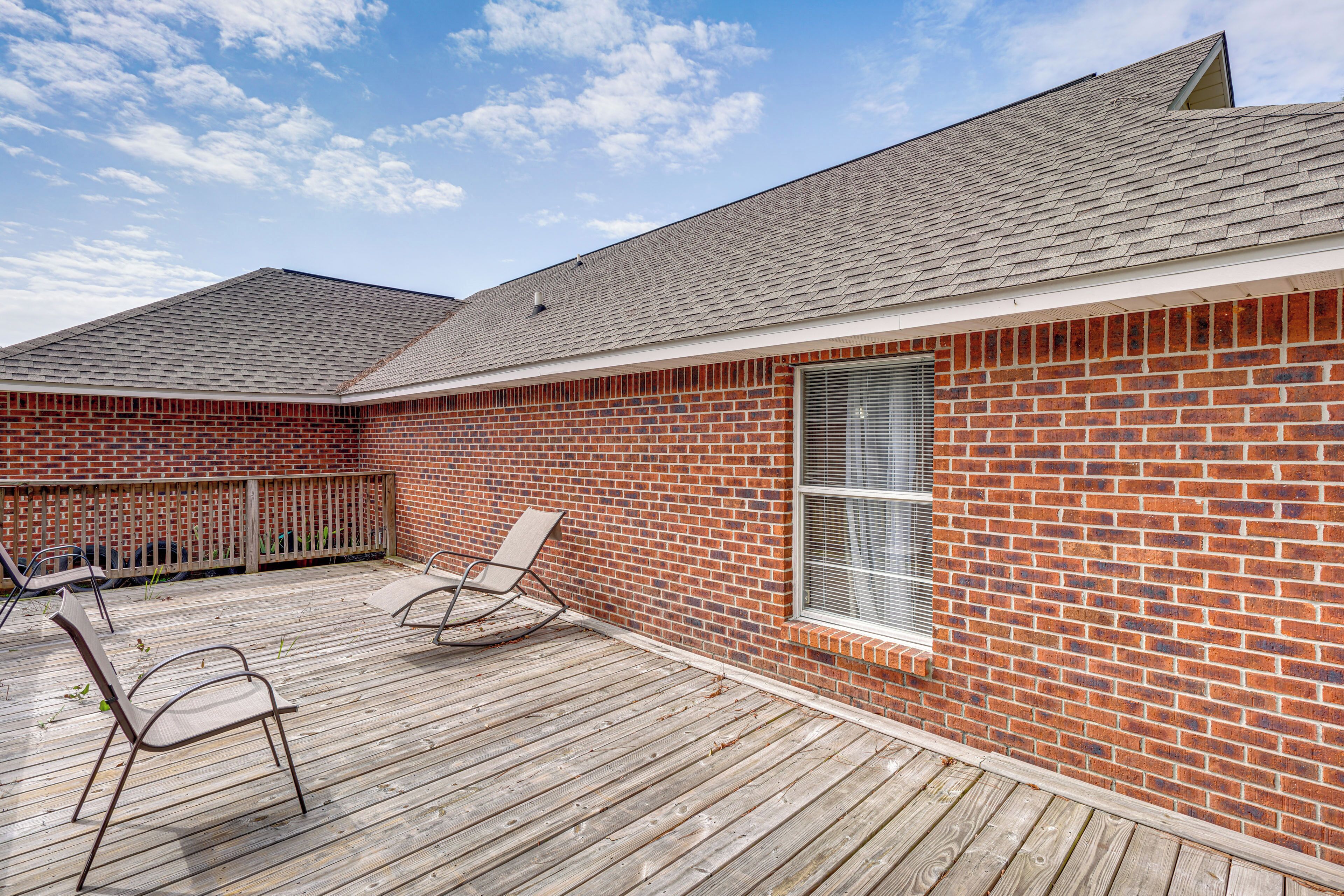 A brick building with a wooden deck, two rocking chairs, and a window.