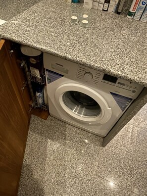 Eine Waschmaschine mit Frontöffnung in einer Küche mit Granit Arbeitsplatten und einem Holzkorpus.